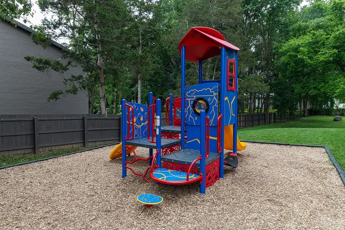 Charming outdoor playground with vibrant blue and red play equipment surrounded by lush greenery, perfect for family fun.