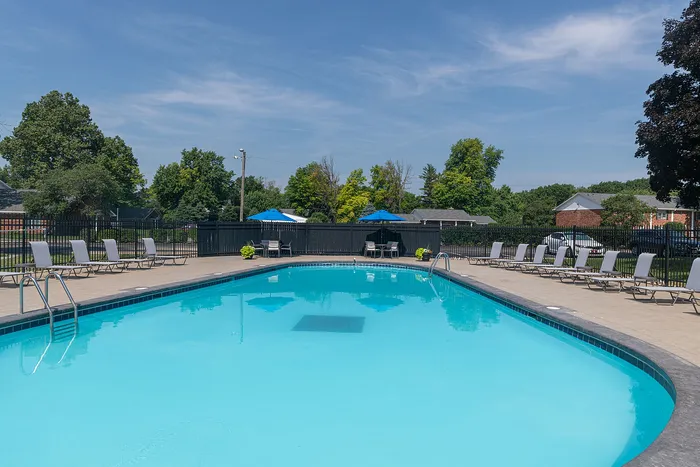 Inviting outdoor pool with lounge chairs and vibrant umbrellas, surrounded by lush greenery under a clear blue sky.