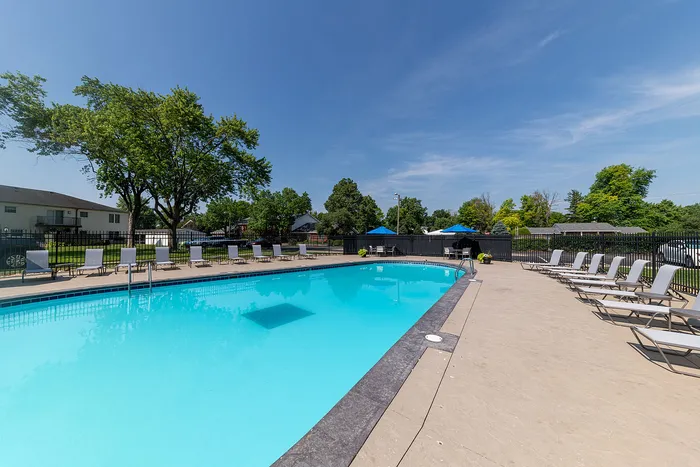 Inviting outdoor pool area with sun loungers set against a backdrop of lush greenery and a clear blue sky.