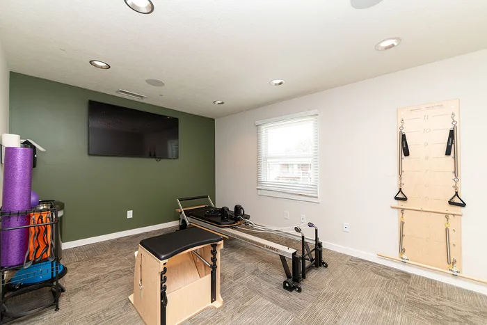 Bright and inviting home gym with modern pilates equipment, green accent wall, and wall-mounted TV.
