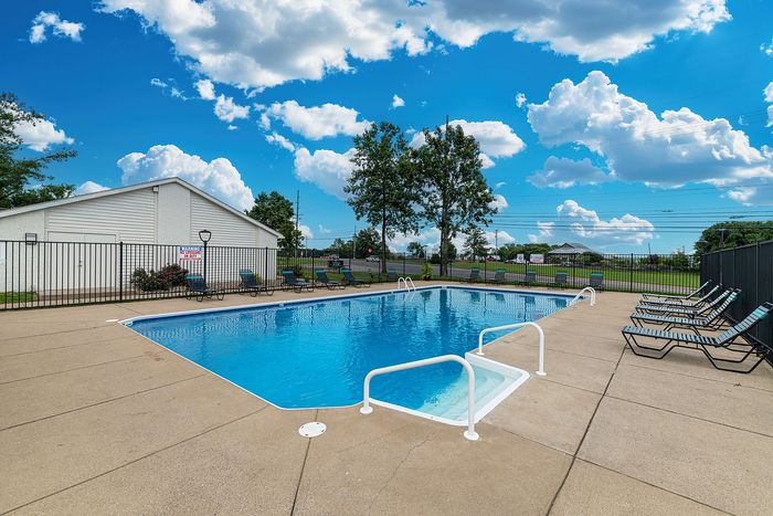 Inviting outdoor pool area with stylish lounge chairs and a serene blue sky backdrop, perfect for relaxation and leisure.