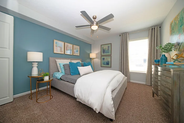 Inviting bedroom with a cozy gray bed, stylish blue accent wall, and elegant decor for a serene and modern atmosphere.