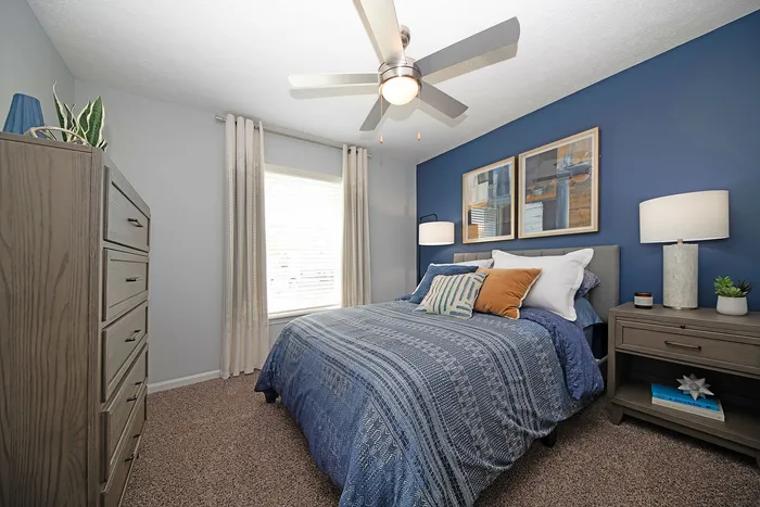 Cozy bedroom with modern blue accent wall, stylish decor, and elegant furnishings, featuring a plush bed and natural light from a large window.