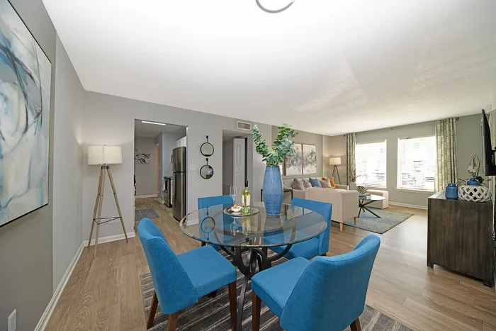 Bright open-concept living space featuring a stylish dining area with blue chairs, modern kitchen, and elegant living room with natural light.