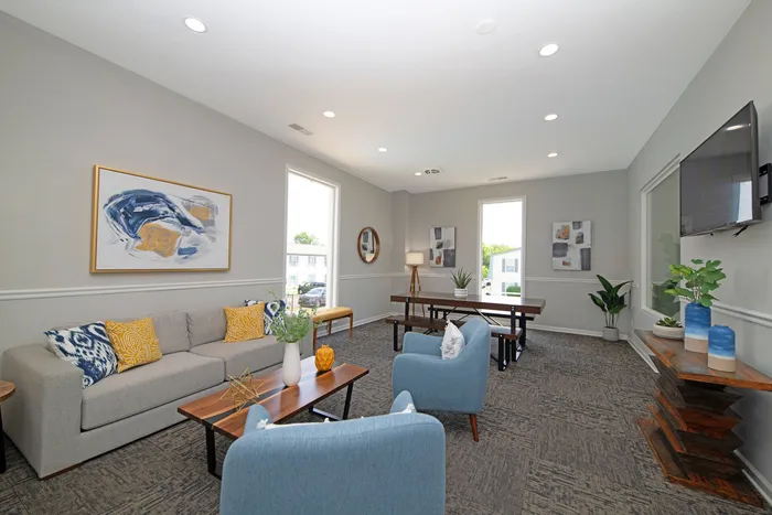 Inviting living room with modern decor, featuring a stylish grey sofa, blue armchairs, abstract artwork, and lush greenery.