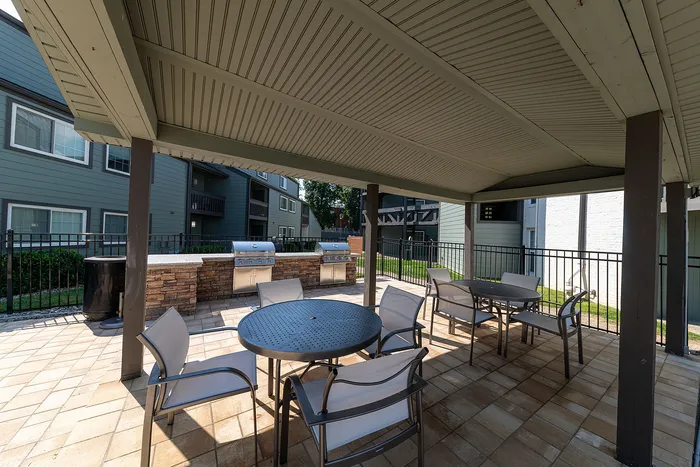 Inviting outdoor seating area under a shaded pergola, featuring modern patio furniture and stainless steel barbecue grills, perfect for entertaining.