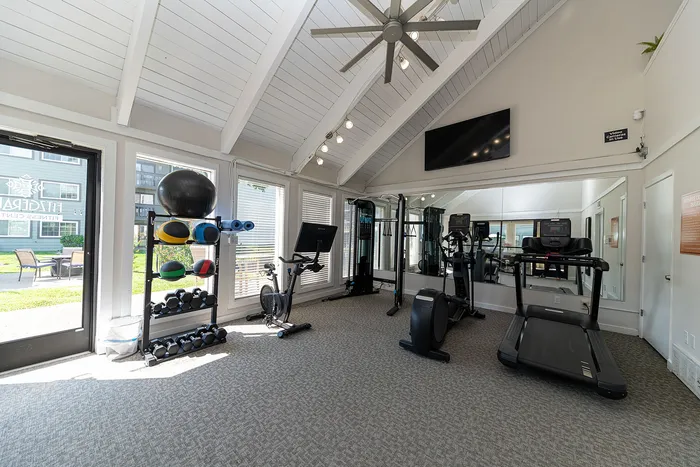 Bright and modern fitness center with high ceilings, featuring treadmills, exercise bikes, and a variety of weights for a comprehensive workout experience.