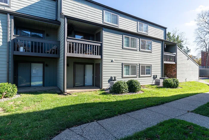 Charming apartment building with private balconies, modern siding, and lush green surroundings against a sunny backdrop.