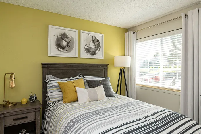 Bright and cozy bedroom with a contemporary design, featuring a striped bedding set, modern artwork, and ample natural light through large windows.