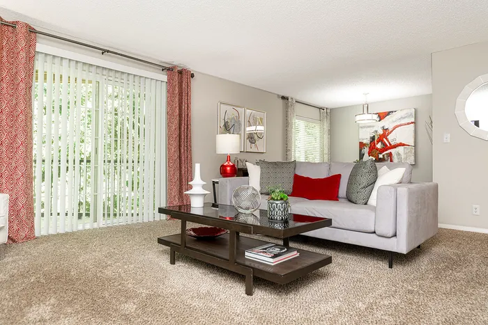 Inviting living room with plush gray sofa, vibrant red accents, and sleek modern decor, bathed in natural light from large sliding doors.