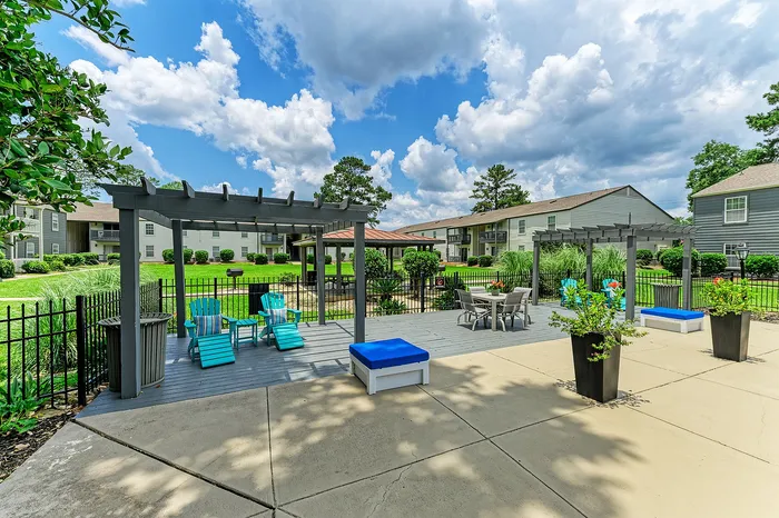 Inviting outdoor space with pergola, cozy seating, vibrant greenery, and clear blue skies at a modern apartment complex.