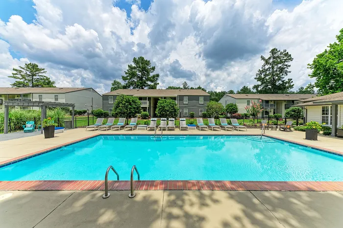 Inviting outdoor pool area with lounge chairs, surrounded by lush greenery and modern apartments, perfect for relaxation.