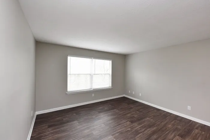 Spacious modern room with sleek wood flooring and large window allowing natural light.