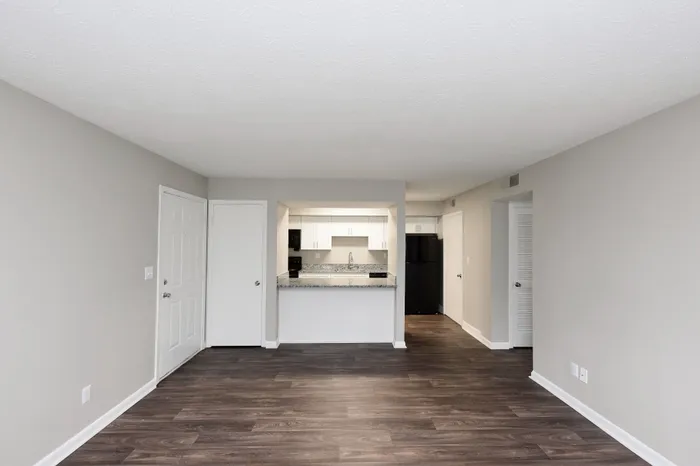 Modern open-concept living area with sleek kitchen, featuring elegant dark wood flooring and bright white cabinetry.
