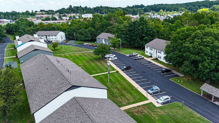 Scenic aerial view of a modern apartment complex surrounded by lush greenery and ample parking spaces, offering a tranquil suburban living experience.