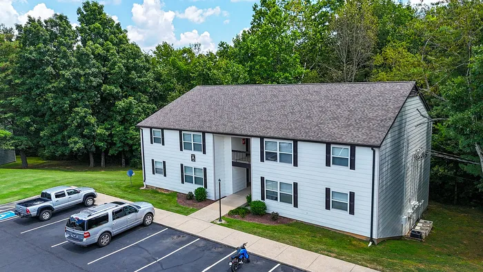 Charming two-story apartment building with ample parking and lush green surroundings, perfect for comfortable living.