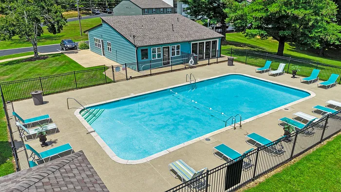 Inviting community pool area with vibrant lounge chairs, surrounded by lush greenery, showcasing a charming clubhouse.
