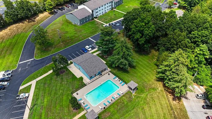 Aerial view of a charming apartment complex with lush greenery, a sparkling swimming pool, and ample parking in a serene neighborhood.