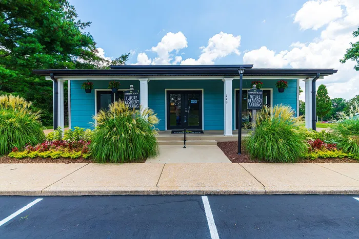 Inviting residential office with vibrant blue facade, lush landscaping, and ample parking, ready to welcome future residents.