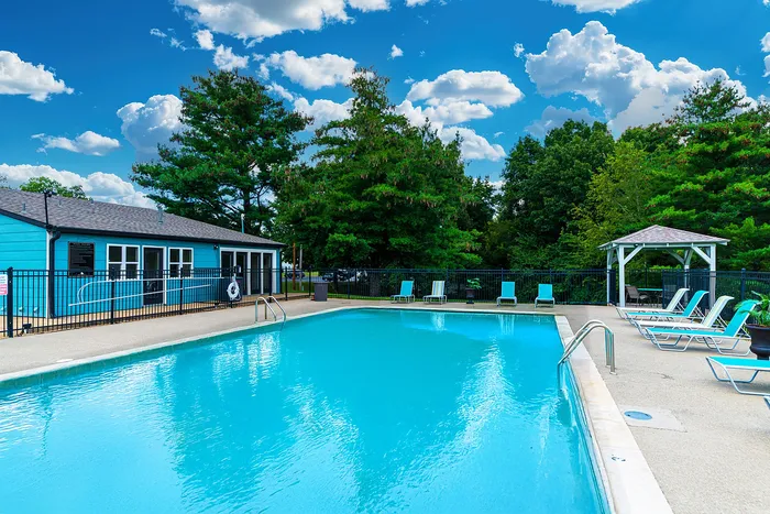 Inviting outdoor pool area with a charming blue clubhouse, surrounded by lush greenery and bright blue skies.