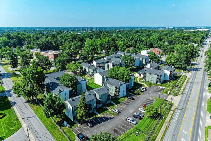 Scenic aerial view of a charming residential community surrounded by lush greenery, featuring modern apartment buildings and ample parking.