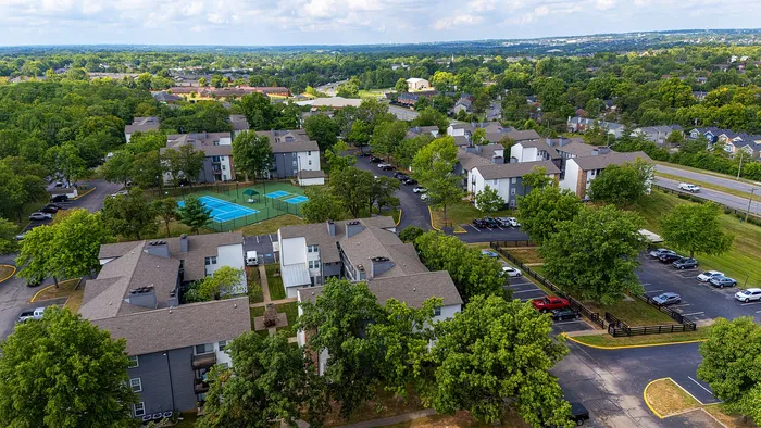 Vibrant aerial view of a modern apartment community with lush greenery, tennis courts, and ample parking nestled in a serene neighborhood.