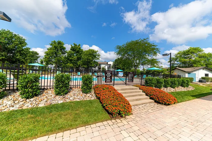Inviting outdoor pool area surrounded by lush greenery and vibrant flowers, perfect for relaxation and leisure under a clear blue sky.