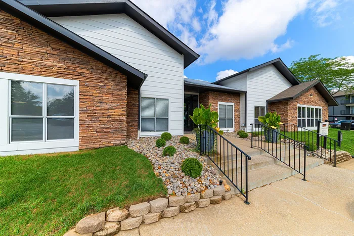 Charming exterior of a modern apartment complex with stone accents, lush landscaping, and inviting walkway.