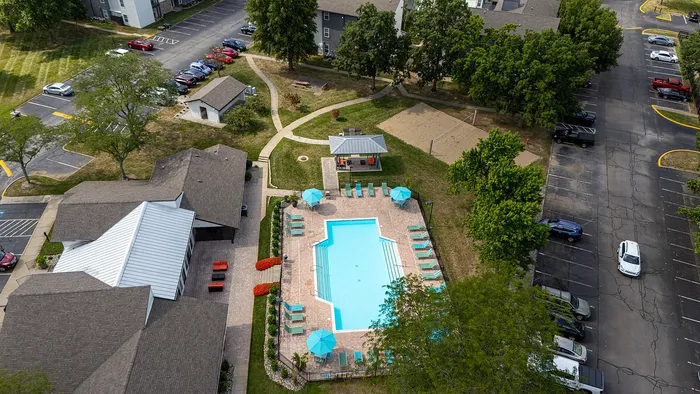 Aerial view of a vibrant community complex featuring a sparkling swimming pool, comfy lounge chairs, and lush greenery, perfect for relaxation and recreation.