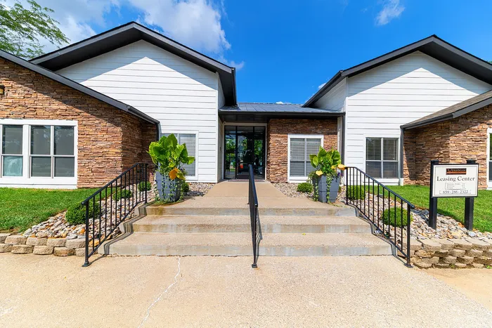 Inviting leasing center entrance with modern design, featuring stone accents and lush greenery under a bright blue sky.
