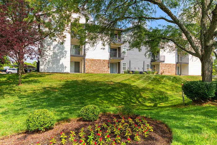 Charming apartment complex with elegant balconies surrounded by lush greenery and vibrant flower beds.