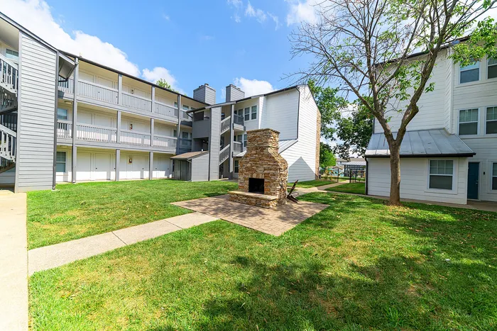 Charming apartment complex courtyard with lush green lawn, inviting stone fireplace, and modern architecture under a clear blue sky.