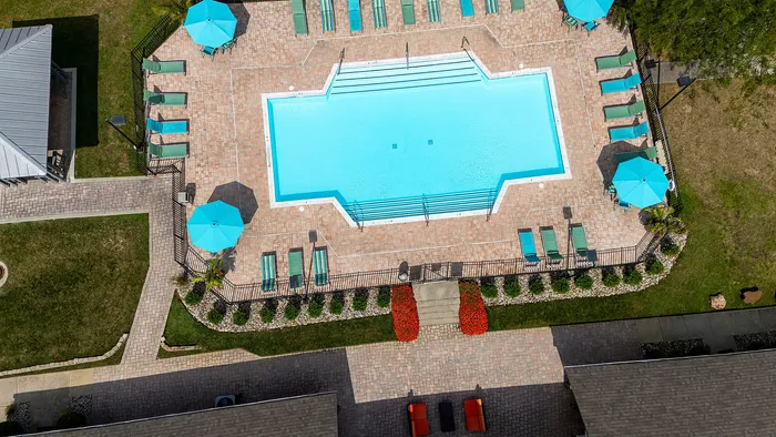 Inviting aerial view of a luxurious pool area with vibrant turquoise umbrellas, surrounded by elegant stone tiles and lush greenery.