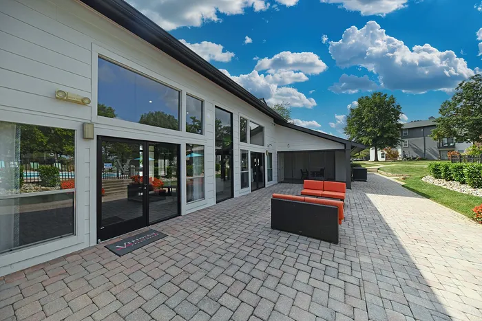 Modern apartment complex patio with stylish seating, lush greenery, and vibrant blue sky, offering a relaxing outdoor space.