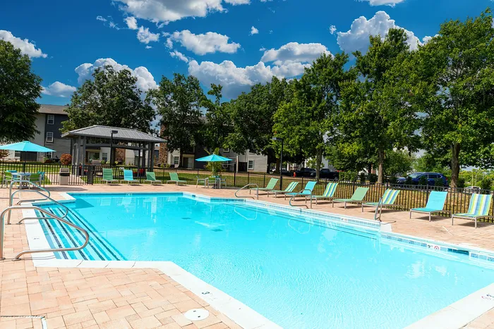 Inviting outdoor pool area with vibrant sun loungers, shaded seating, and lush greenery, perfect for relaxation and leisure under a sunny sky.