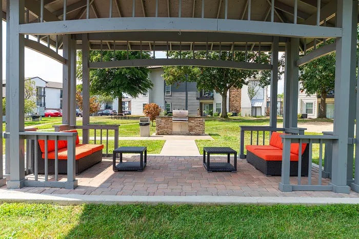 Charming outdoor pavilion with vibrant orange-cushioned seating, perfect for relaxation and entertaining, featuring a modern grill station amidst lush green surroundings.
