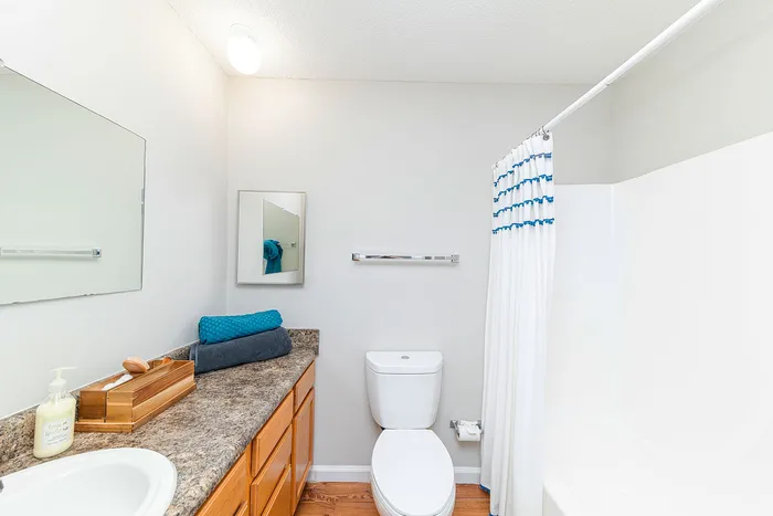 Elegant bathroom featuring a pristine white bathtub, chic marble countertop with wooden cabinets, and modern fixtures accented by soft lighting.