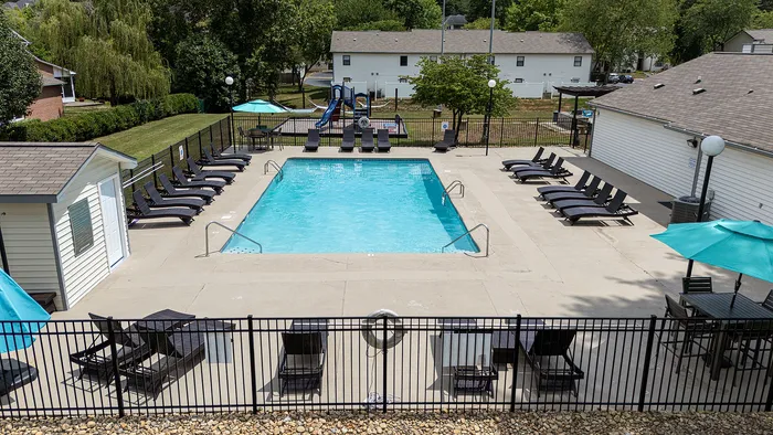 Inviting outdoor pool area with modern lounge chairs, surrounded by lush greenery and a play area, perfect for relaxation and family fun.