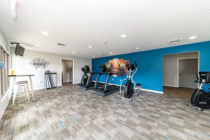 Bright, modern gym featuring treadmills and exercise bikes against a vibrant blue accent wall with motivational decor.