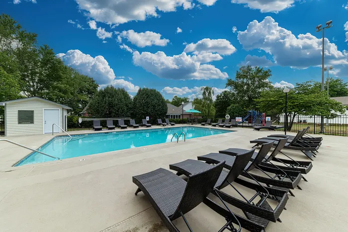 Inviting swimming pool area with modern lounge chairs and lush greenery under a vibrant blue sky.