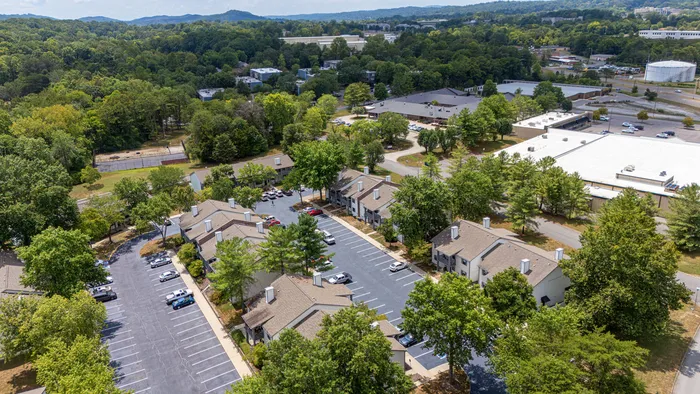 Scenic aerial view of a charming apartment complex surrounded by lush greenery and ample parking, offering a peaceful residential environment.