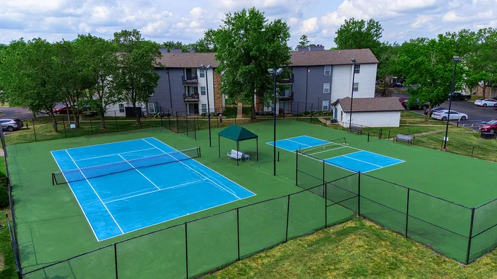 Inviting apartment complex with vibrant blue tennis courts surrounded by lush greenery and modern residential buildings.