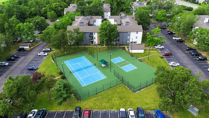Aerial view of a vibrant apartment complex featuring well-maintained tennis courts surrounded by lush greenery and ample parking.