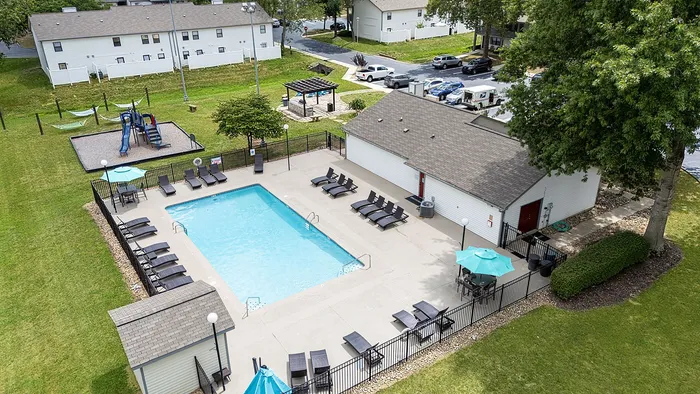 Inviting apartment complex featuring a pristine swimming pool, relaxing lounge chairs, a charming gazebo, and a delightful playground area set amidst well-maintained green spaces.