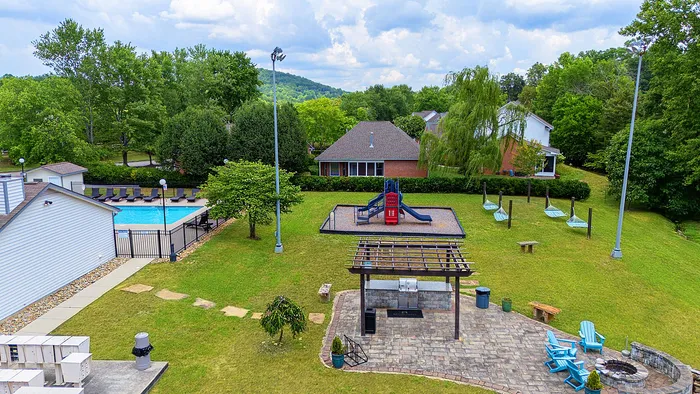 Inviting outdoor community space features a sparkling pool, vibrant playground, and cozy fire pit area surrounded by lush greenery.
