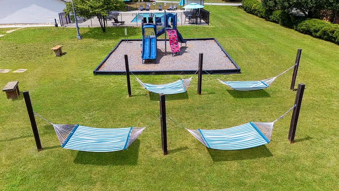 Tranquil outdoor space with striped hammocks, vibrant playground, and lush green lawn, perfect for family relaxation.