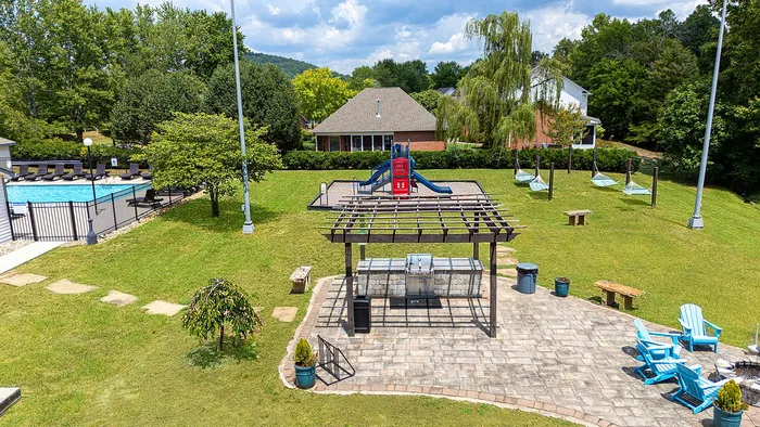 Charming outdoor community space featuring a playground, swimming pool, and a cozy BBQ area with Adirondack chairs, perfect for relaxation and fun in a serene setting.
