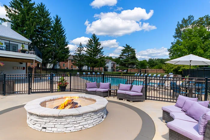 Inviting outdoor space with cozy seating around a fire pit, a large pool, and lush green surroundings on a sunny day.