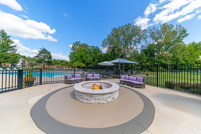 Elegant outdoor lounge area with a stone fire pit, cozy seating, and a pristine pool backdrop surrounded by lush greenery.