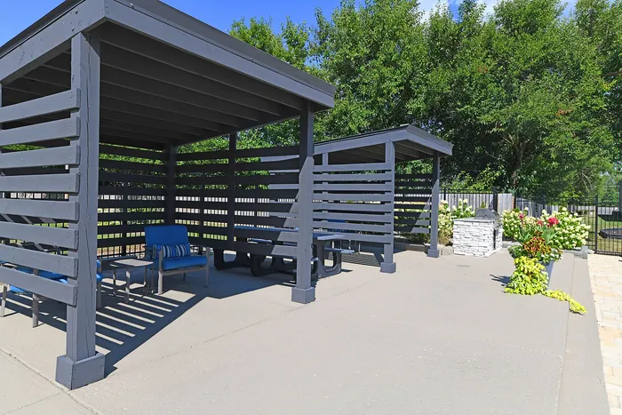 Chic outdoor seating area with modern pergolas, lush greenery, and cozy blue chairs, perfect for relaxation and social gatherings.